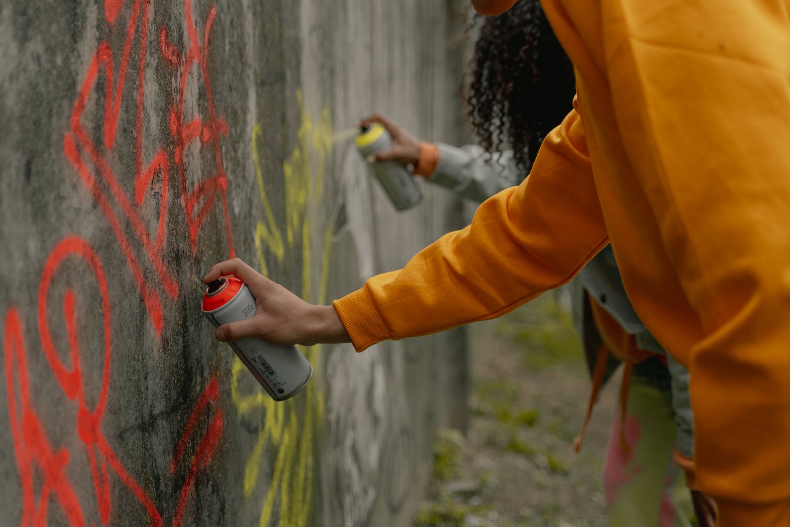 A Person in Yellow Long Sleeve Shirt Spray Painting a Wall